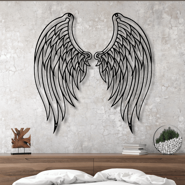 Metal angel wings wall decor on a textured wall above a wooden surface.