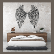 Metal angel wings wall art above a bed in a bedroom setting.