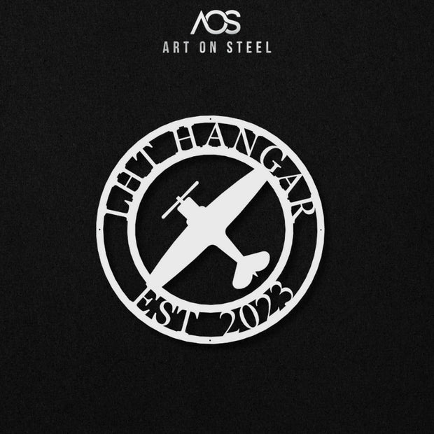 A white circular metal sign featuring a single-propeller airplane in the center. The sign is framed with the text "LHT HANGAR" at the top and "EST 2023" at the bottom. The art is shown against a dark, black background, and the "Art on Steel" logo is visible at the top.