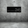 A rectangular house number metal wall art plaque with the inscription 'Park Avenue 245' mounted on a grey textured wall. Art on Steel