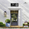 Gray door with decorative house number plate on a white brick wall, from Art on Steel.