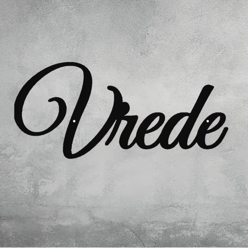 A close-up of a decorative, black metal wall art piece that spells out the word "Vrede" in an elegant script font. The sign is mounted on a gray, distressed concrete wall. Art on Steel