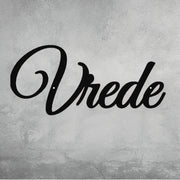 
A close-up of a decorative, black metal wall art piece that spells out the word "Vrede" in an elegant script font. The sign is mounted on a gray, distressed concrete wall. Art on Steel