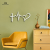 
A close-up of a modern, white steel wall art piece that combines a cross, a heartbeat line, and a heart to symbolize faith, hope, and love. The art hangs on a sage green wall above a bright yellow armchair and a matching yellow dresser. The "Art on Steel" logo is visible in the top left corner