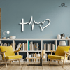 
A set of two images featuring a decorative metal wall art piece that symbolizes faith, hope, and love with a cross, a heartbeat line, and a heart. The first image shows a black version of the art hanging on a white wall above a beige armchair, while the second shows a white version on a blue-gray wall centered above a white bookcase with two yellow chairs. The "Art on Steel" logo is visible in the top right corner of both images