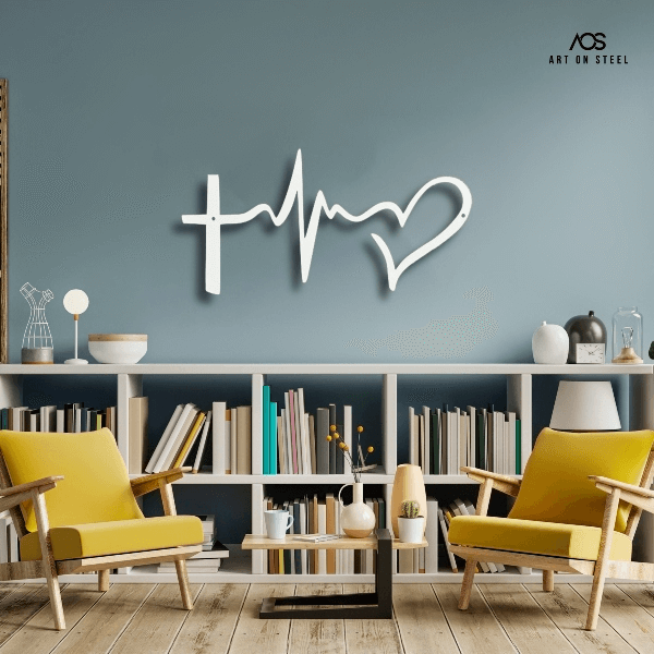 
A set of two images featuring a decorative metal wall art piece that symbolizes faith, hope, and love with a cross, a heartbeat line, and a heart. The first image shows a black version of the art hanging on a white wall above a beige armchair, while the second shows a white version on a blue-gray wall centered above a white bookcase with two yellow chairs. The "Art on Steel" logo is visible in the top right corner of both images